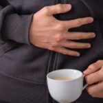 Person holding stomach in pain after drinking coffee